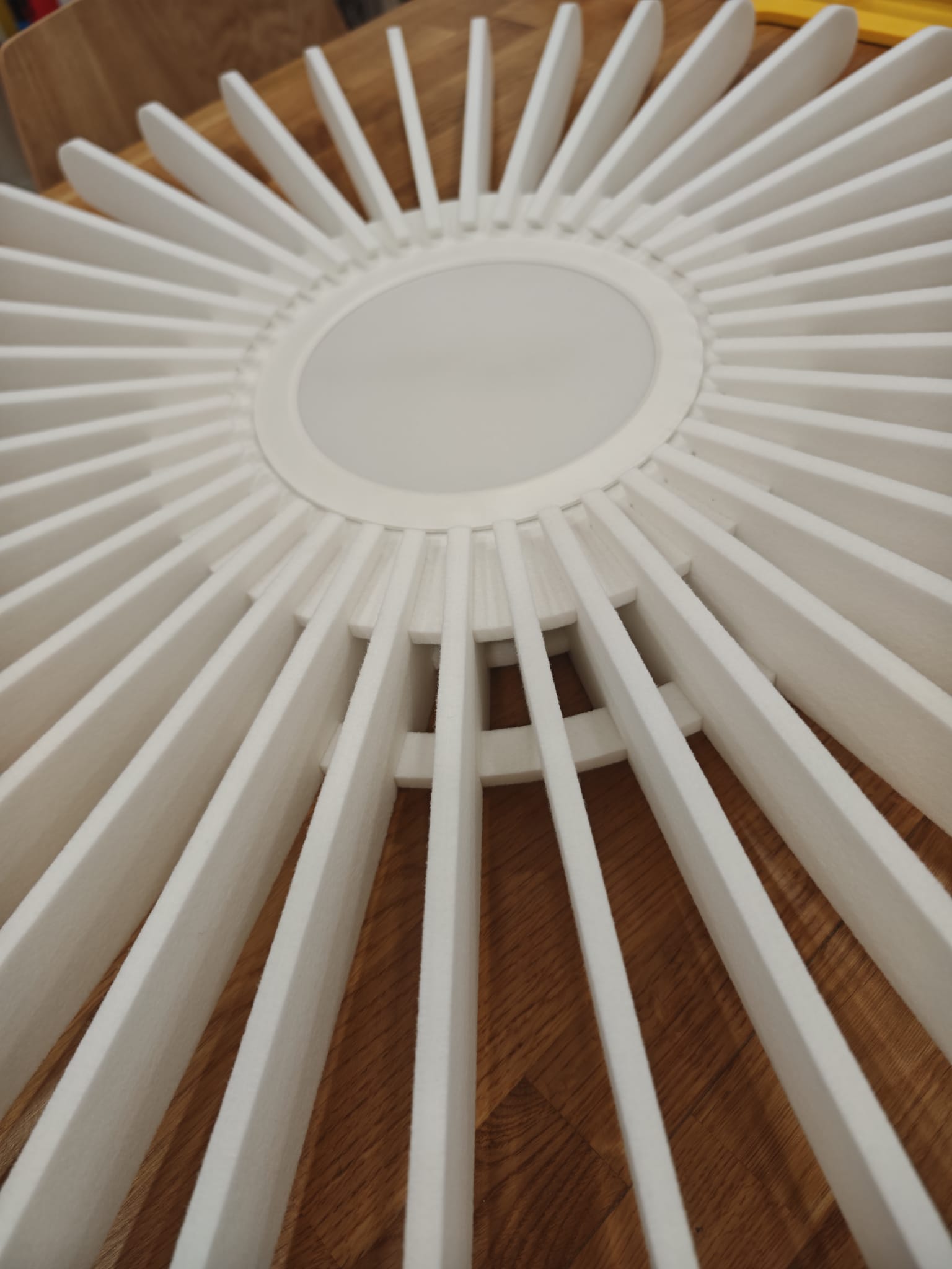Vue en perspective d'un Solea en cours d'assemblage : les lamelles blanches en feutre PET rayonnent autour du disque central, posé à plat sur une table en bois clair.